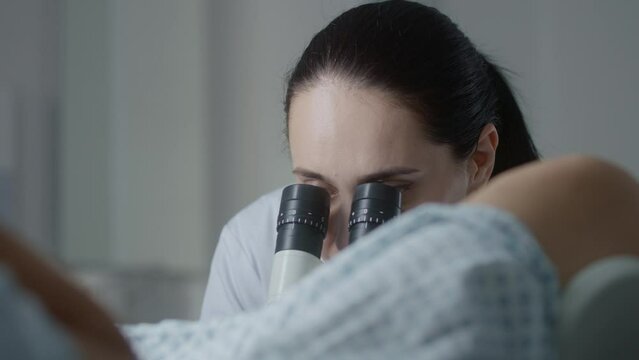 Gynecology room in modern hospital. Female gynecologist uses colposcope, takes tests from patient and talks. Woman lies on gynecological chair during colposcopy procedure. Preparation for pregnancy.