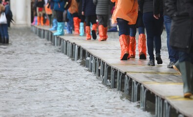 people in gaiters boots walking over elevated walkway during high tide Venice Italy