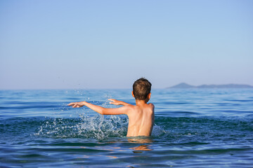 Blond Boy's Joyful Splash: End-of-Summer Fun on a Greek Beach with water flying around