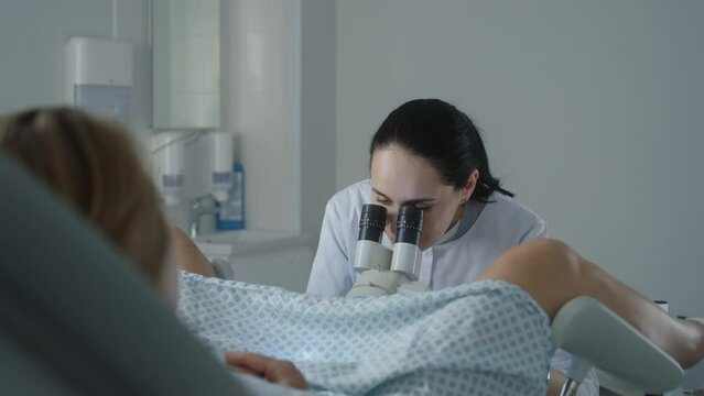 Gynecology room in modern clinic. Female gynecologist uses colposcope, takes tests from patient. Woman lies on gynecological chair during colposcopy procedure. Preparation for pregnancy. Slow motion.