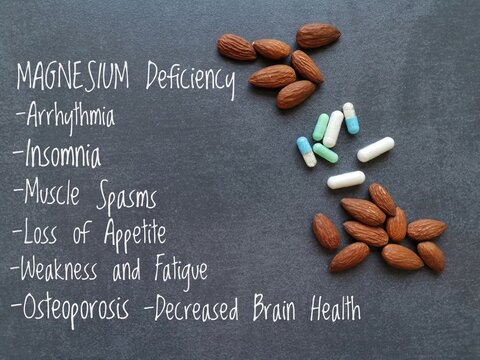 Symptoms and signs of magnesium deficiency written on the notebook, with almond and pills in background. Low magnesium level may cause weakness, fatigue, osteoporosis, muscle spasms, arrhythmia, etc.