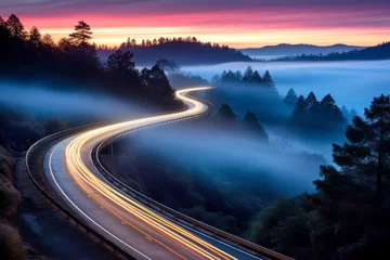 Foto op Canvas Car headlights and traffic lights on a winding road through pine trees, in a foggy valley at sunset, captured by long exposure photography © mozZz