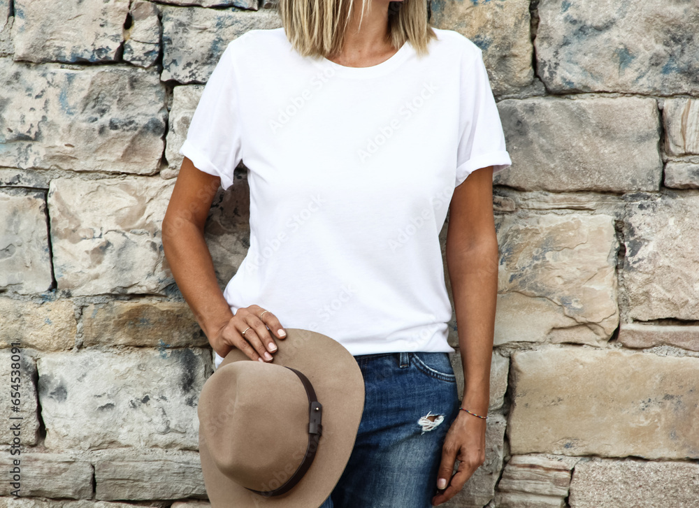 Wall mural Girl wearing blank white tshirt with copy space for your text or design. White t-shirt mock up with hat on natural stone wall background