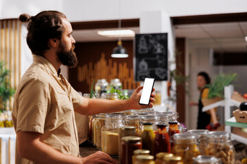 Client in zero waste shop using mockup mobile phone to videocall his wife, buying her healthy food. Customer with isolated screen smartphone phone calls partner over internet in local supermarket - obrazy, fototapety, plakaty