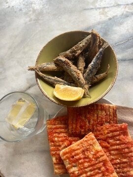 Bread with tomato spread, fried small fish in a bowl and a glass of water with lemon, spanish tapas snacks on marble table