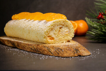Delicious tangerine cake roll with vanilla buttercream filling on wooden plate, holiday winter dessert