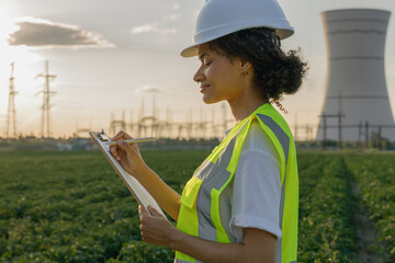 Female engineer constructor stands with clipboard on field on industrial enterprise background