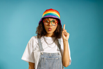 Portrait of pensive young woman holding index finger up with great new idea on blue background
