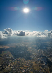 Aerial view from airplane window at high altitude of distant city covered with puffy cumulus clouds...