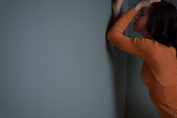 a woman with dark hair and orange clothes in depression and despair turned her face to the gray wall