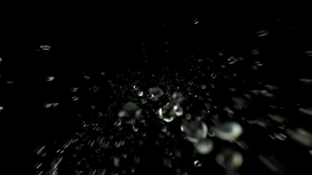 Bottom view isolated slow motion macro shooting capturing lots of clear water drops of different sizes falling down to the camera from above. Black background.