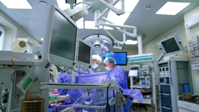 Well-equipped surgery room in modern hospital. Uniformed surgeons perform operation at backdrop in blur.