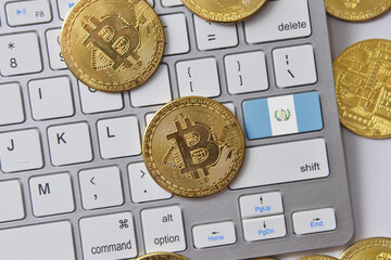 national flag of guatemala on the keyboard with bitcoin coins on a grey background.