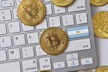 national flag of argentina on the keyboard with bitcoin coins on a grey background.