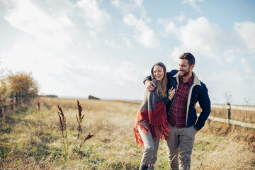 Young couple having a stroll on a grassland in the countryside - obrazy, fototapety, plakaty