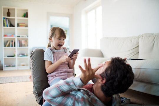 Young girl taking a picture of her father on the smartphone in the living room at home