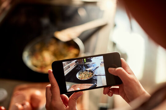 Close up of a young woman taking a picture on a smartphone of the meal she prepared in the kitchen