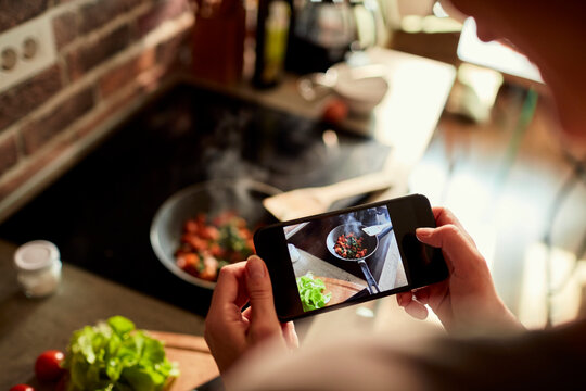 Close up of a young woman taking a picture on a smartphone of the meal she prepared in the kitchen