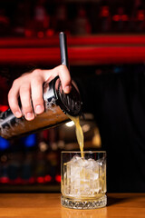 Bartender's hand pours an alcoholic cocktail from a shaker into a glass glass with ice.  Concept of nightclub, bar, karaoke