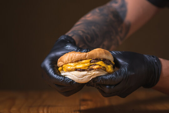  Hand with black gloves holding a tasty juicy burger on a wooden table
