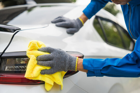 close-up shot of a hand wiping a car's windshield with yellow microfiber cloth, mechanic's hand polishing car hood with soft cloth