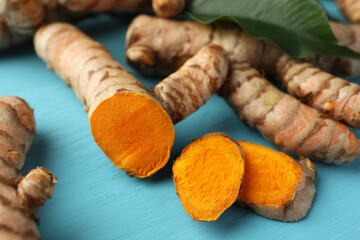 Whole and cut turmeric roots on light blue wooden table, closeup