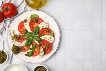 Plate of delicious Caprese salad with pesto sauce on white tiled table, flat lay. Space for text