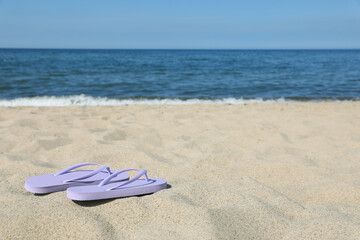 Stylish violet flip flops on beach sand, space for text
