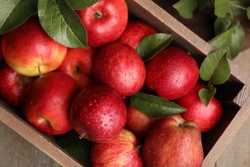 Crate with wet red apples and green leaves on table, top view