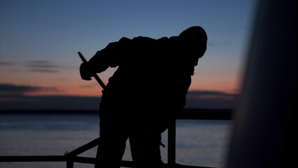 Man cleans deck of fishing boat. Clip. Shadow of man sweeping on ship at dusk. Man cleans up on...