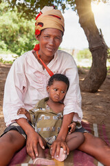 a happy bushmen San woman from Central Kalahari, holding her child, village New Xade in Botswana,...