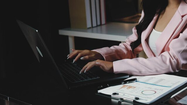 Young Asian woman sitting working in a company office at night, business woman working overtime, working overtime due to heavy workload, working after normal working hours. Overtime concept.