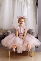 Portrait of a fair-haired girl 7-8 years old in a fluffy lace dress of pale pink color and with a large bow on her head in a dress boutique