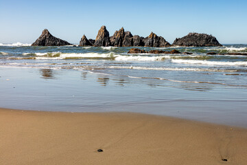 Reflections in sand and surf of lava rocks offshore in the Pacific coast of central Oregon in...
