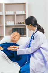 Obraz premium Caring female doctor provides attentive medical care to asian people elderly man lying in hospital bed, highlighting importance of expert healthcare and support during times of illness.