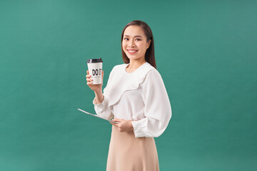 Attractive woman wearing shirt holding tablet and drinking takeaway coffee over green background