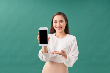Young beautiful attractive Asian woman show blank screen mobile phone isolated on green background