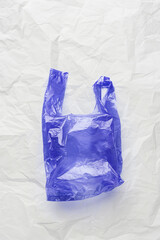 Plastic free concept, top view blue crumpled plastic bag crumpled on white wrinkled paper background. Disposable polythene packet for food. Eco trend minimal style photo, vertical photo, above