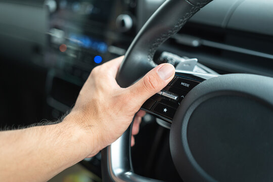 Action of a driver hand is handling on the multi-functional steering wheel during driving a car. Transportation in action photo, selective focus.