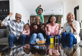 Excited african american parents, son, daughter and grandparents watching sport on tv, slow motion