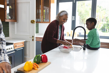 Happy african american grandmother and grandson washing vegetables in kitchen, slow motion - Powered by Adobe