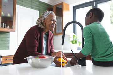 Happy african american grandmother and grandson washing vegetables in kitchen, slow motion
