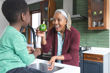 Happy african american grandmother and grandson washing vegetables in kitchen, slow motion