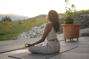 Girl practices outdoor yoga meditation in nature. On the horizon the sunset with its light illuminating her face.