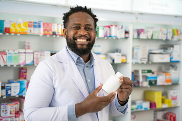 Male doctor looking to camera with smiling at pharmacy. He holding medicine in hand at pharmacy shop. Healthcare, Retirement, Volunteer, Caregiver and Lifestyle concept. - obrazy, fototapety, plakaty