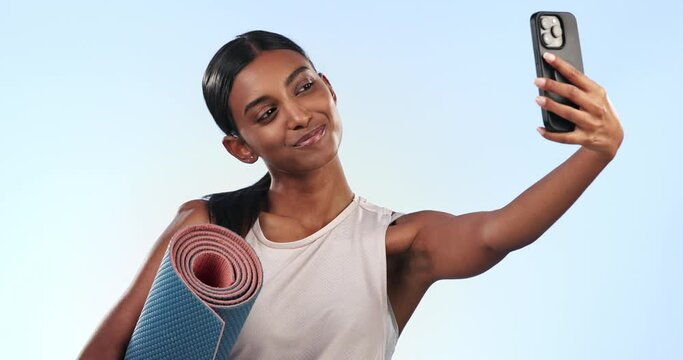 Indian woman, selfie in the gym and yoga with exercise mat, memory for social media and happy on blue background. Fitness, pilates and training with smile in profile picture and influencer in studio