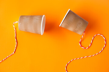 DIY paper cups with string on orange background. Concept, telephone toys which apply with science...