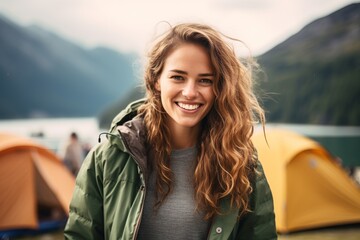 Portrait of a smiling woman against the background of a tent camp on a mountain lake in the morning