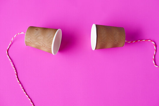 DIY paper cups with string on pink background. Concept, telephone toys which apply with science knowledge about vibration sound through straining strings causing us to hear the sound.   