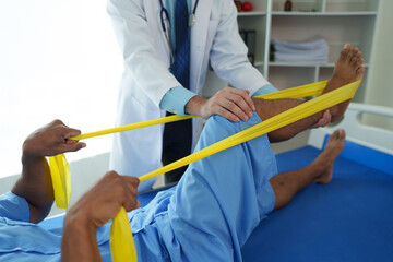 Physical therapist gives resistance band therapy to the legs and knees of an athletic male patient. Physical therapy concept
